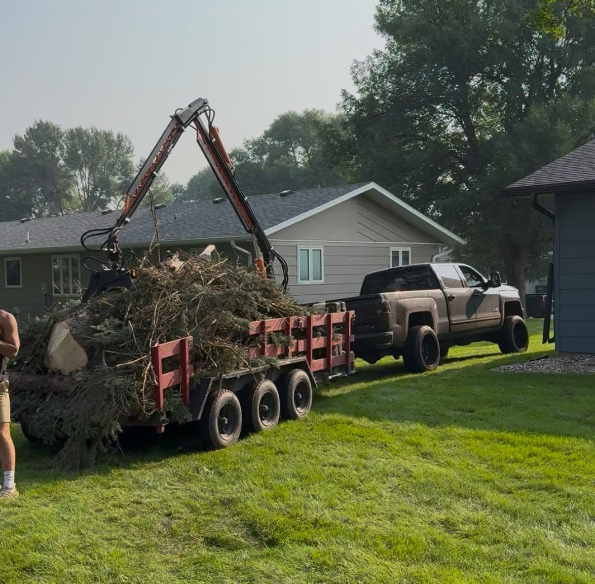The grapple loader swinging a load of brush onto the trailer in a residential yard