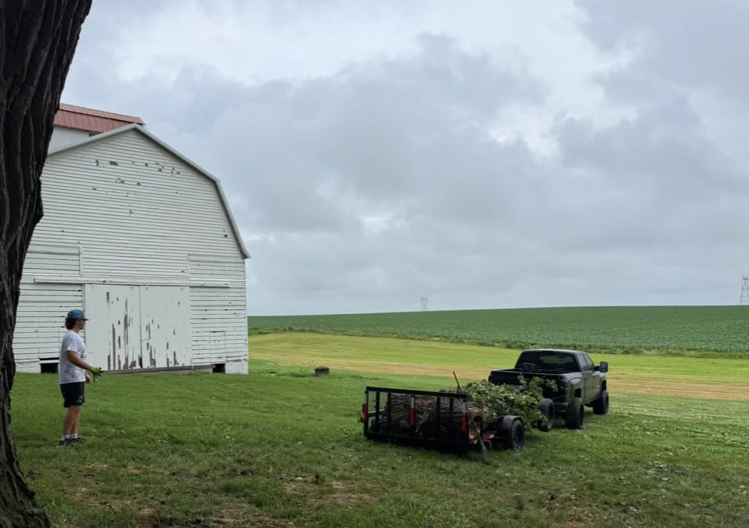 A crew member loading storm brush onto the trailer beside a white barn
