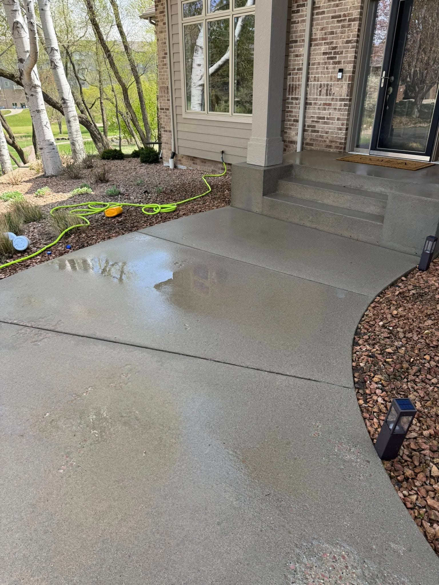 A freshly pressure-washed concrete walkway still wet in front of a brick home